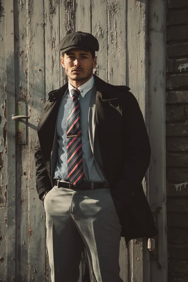 Andreas Schmid, flat cap, coat and tie against a wooden wall
