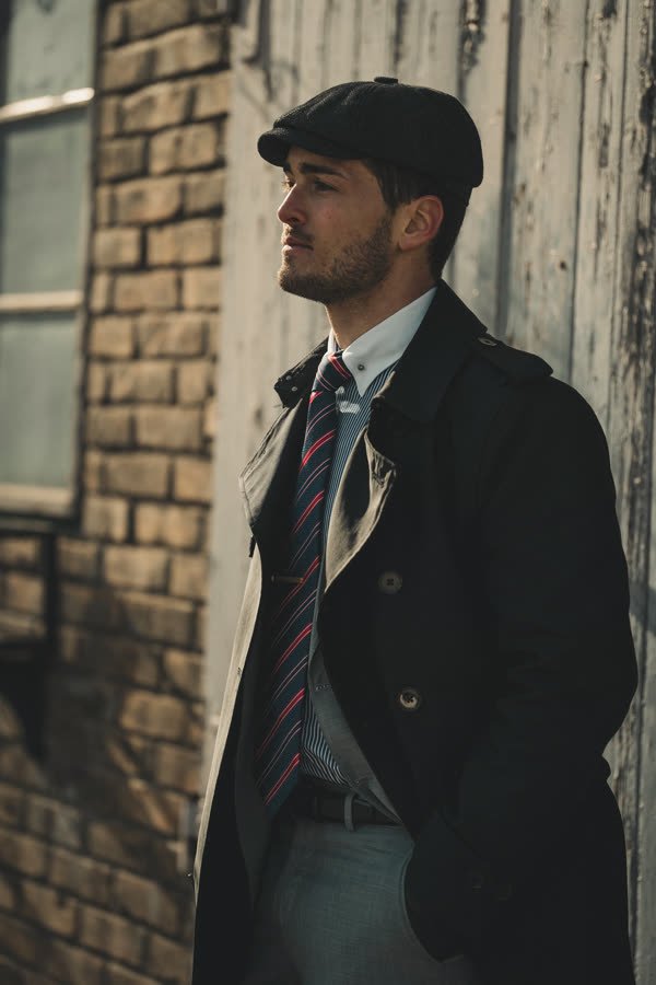 Andreas Schmid, flat cap and dark coat against a brick wall