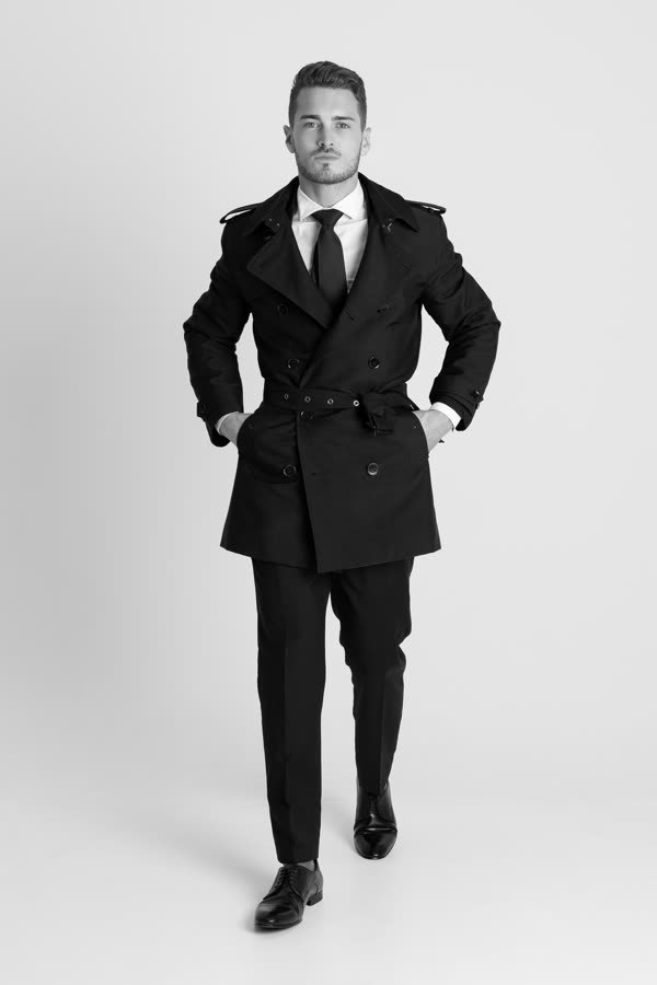 Andreas Schmid, black and white studio photo in a belted trench coat